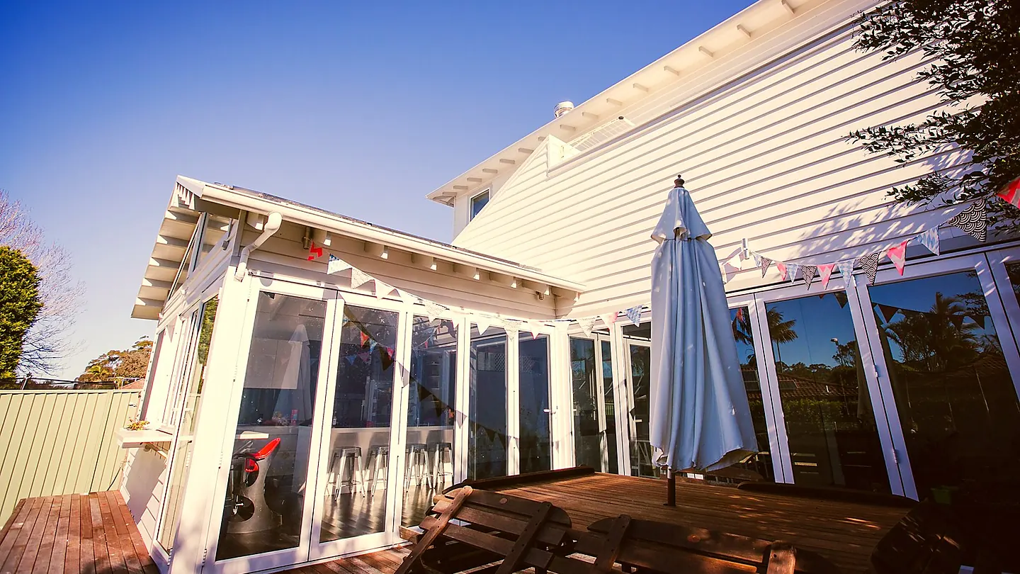 A weatherboard rear addition opening onto a timber deck with an umbrella and outdoor seating.