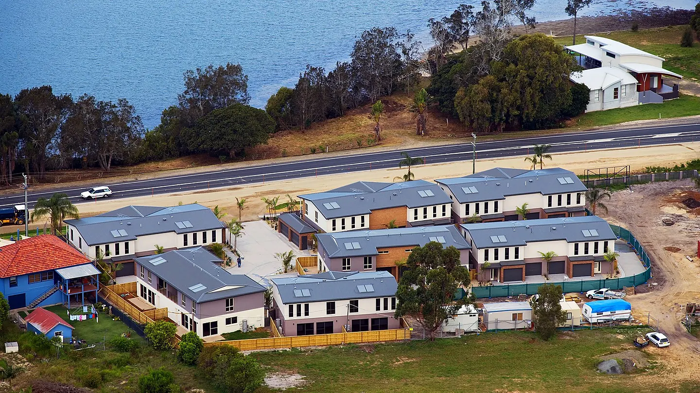 An aerial view of a group of detached dwellings at roofing stage, with driveways formed and landscaping not yet started.