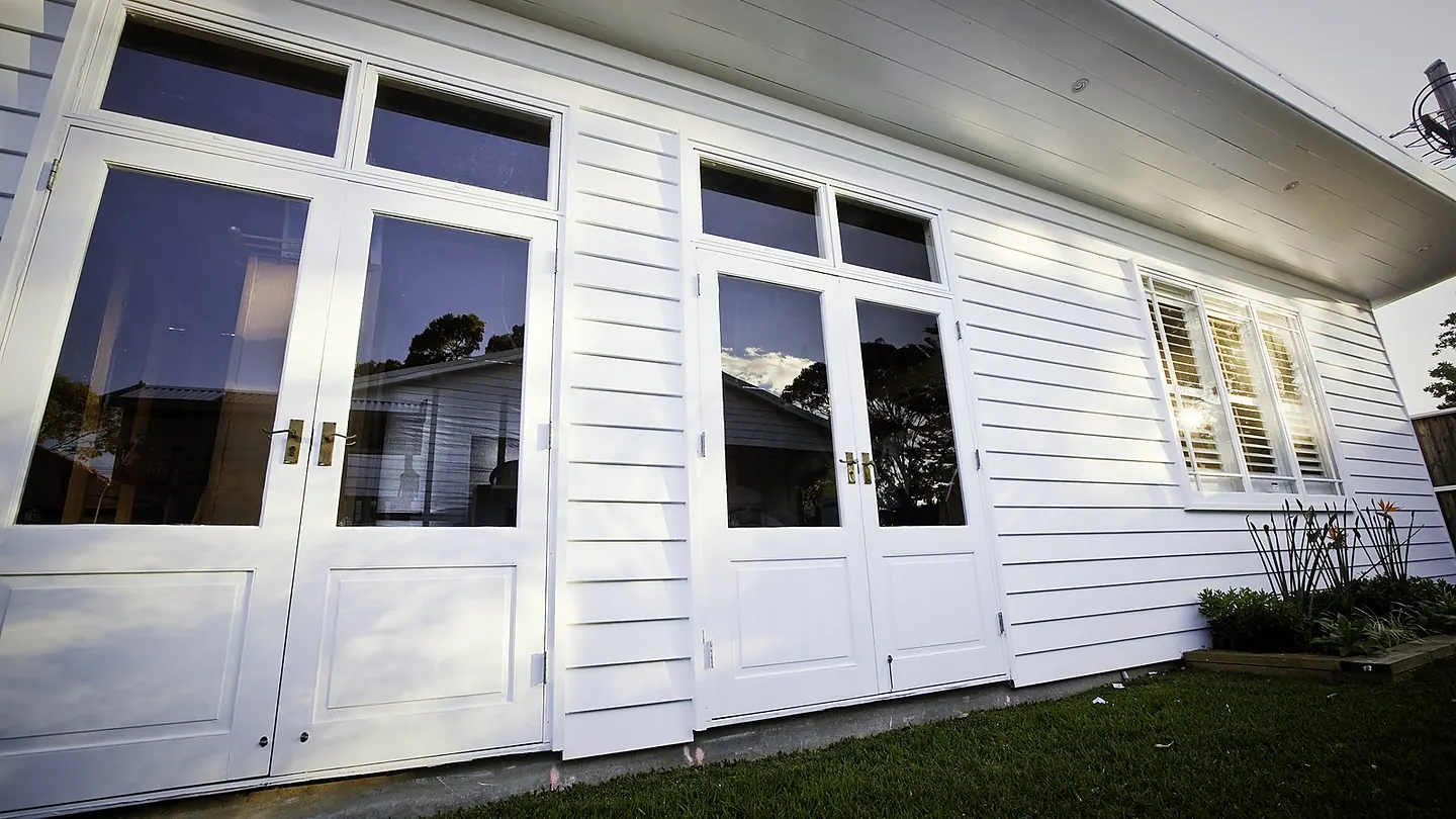 A weatherboard elevation with a continuous bank of white french doors and highlight windows above.