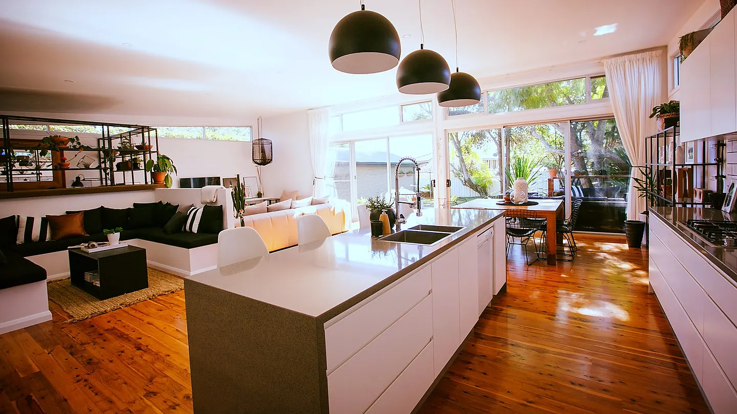A kitchen island under pendant lights, with clerestory glazing above the benches and timber floors running through to the living area.