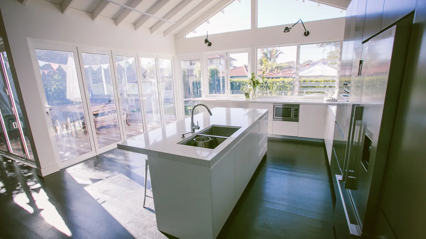 Kitchen island beneath exposed rafters and clerestory glazing, opening to a garden.