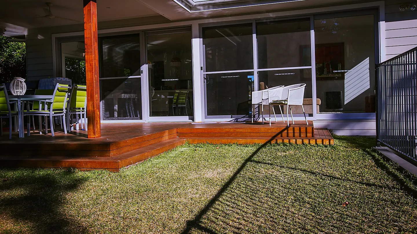 The rear of a clad two storey house with a raised timber deck and lawn running to the boundary.