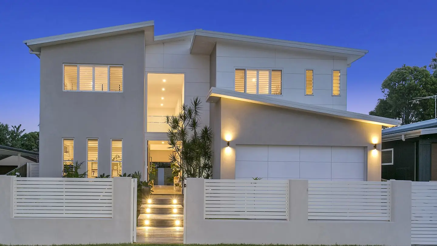 A rendered two-storey house photographed from the street at dusk, windows lit.
