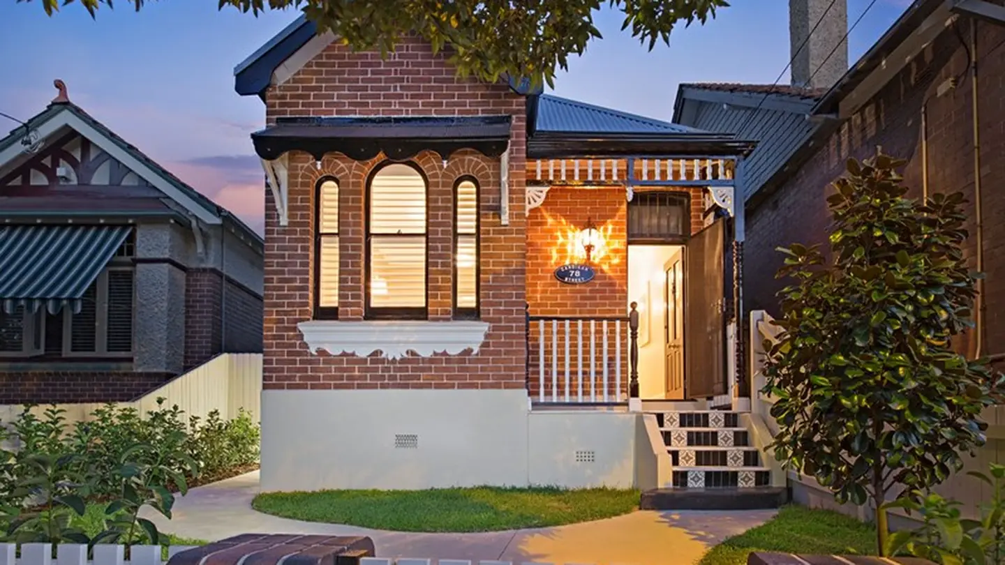 A period brick house lit at dusk, sitting between its neighbours on a suburban street.