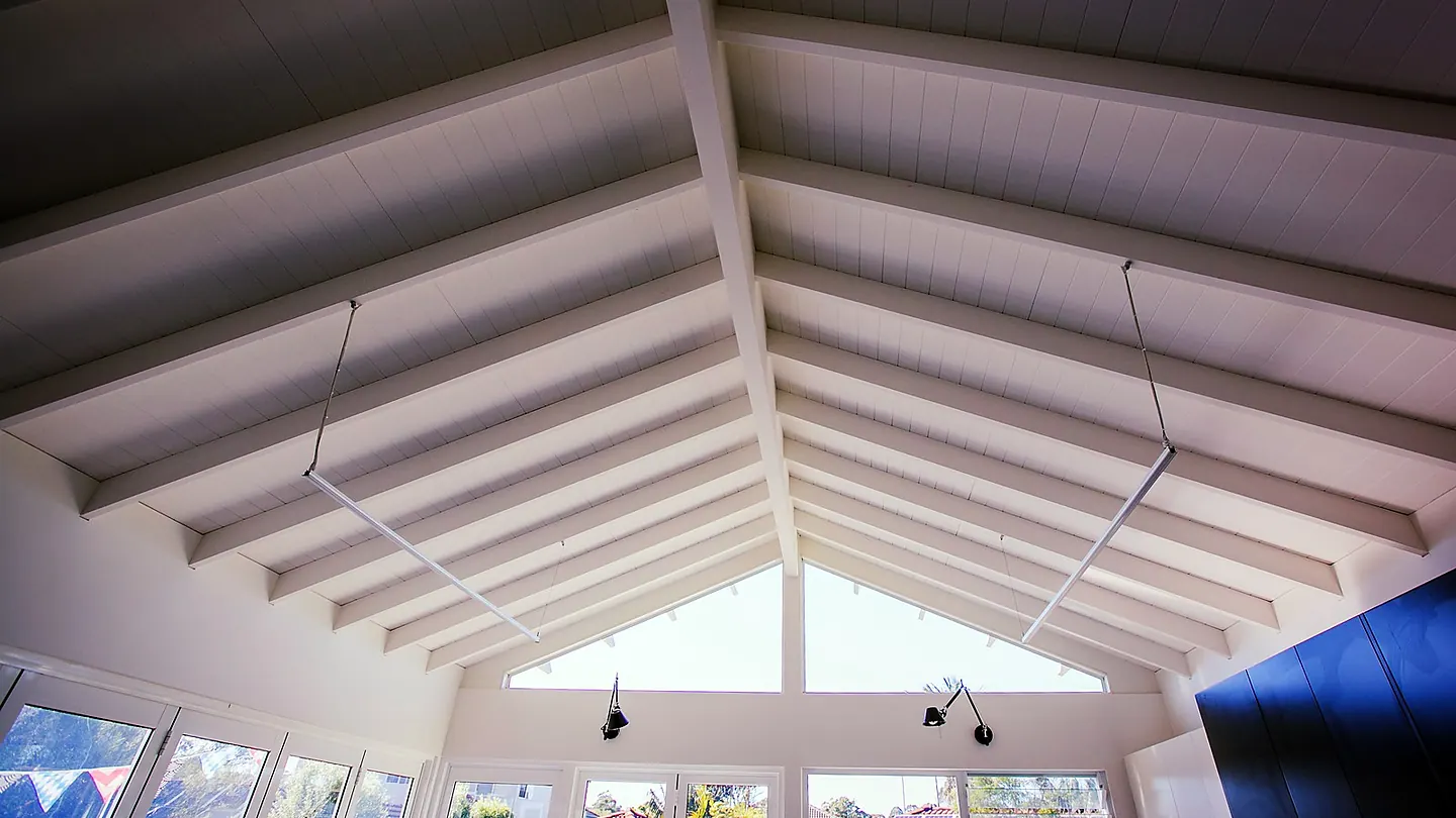 Exposed white rafters rising to a ridge above a glazed gable end, seen from below.