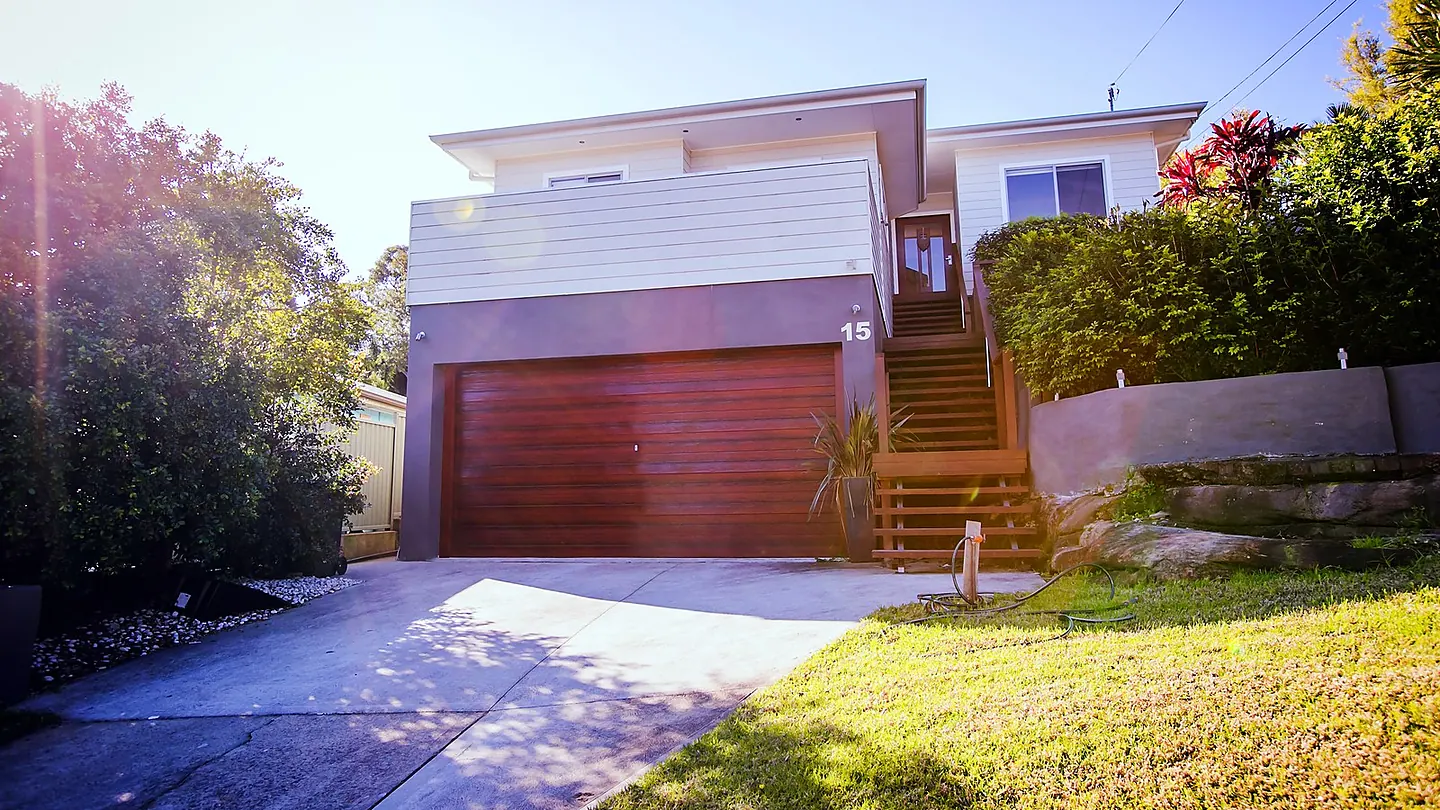 A two storey clad house on a sloping block, seen from the street, with a double garage under the upper floor and timber stairs to the entry.