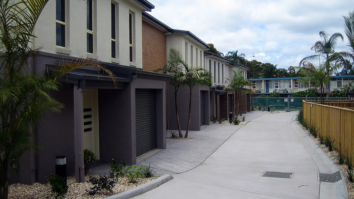 A shared driveway running between two rows of attached dwellings, with garages to each and planting along the edges.