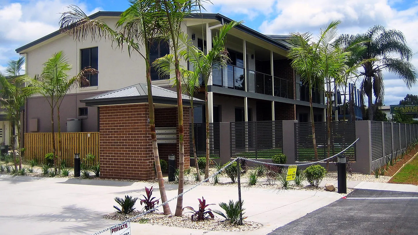 A row of attached two storey dwellings with balconies and planted front setbacks, seen from the street.