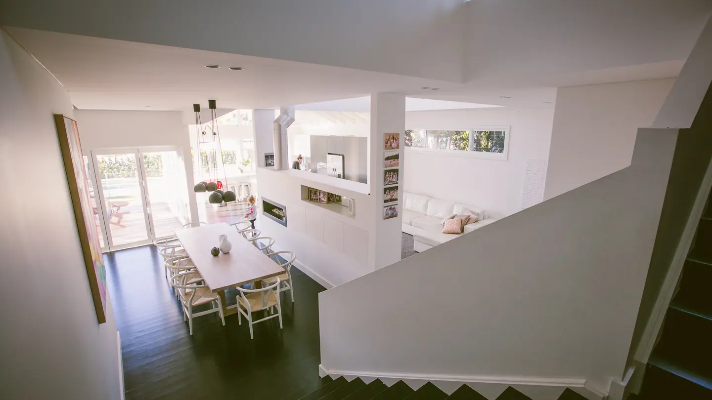 Open-plan living and dining under a double-height void, seen from the stair landing.